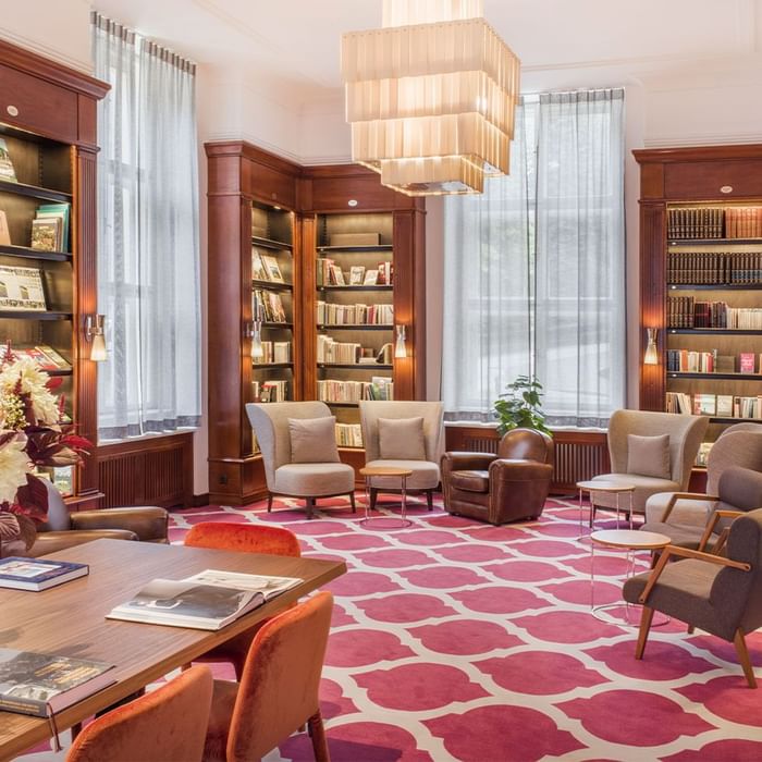 Elegantes Bibliothekszimmer mit gemustertem Teppich, Holzmöbeln, Bücherregalen und gemütlichen Sitzbereichen.