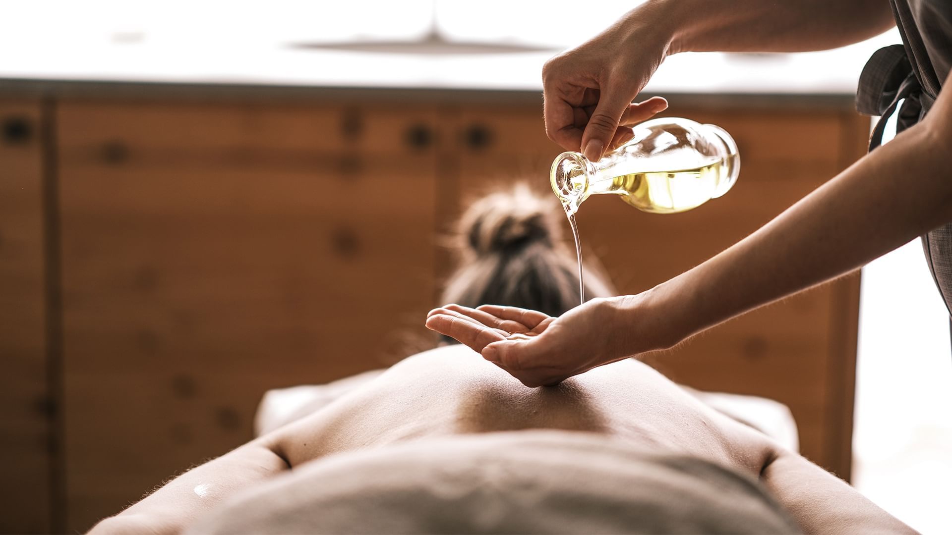 Eine Person gießt Öl auf den Rücken einer anderen Person während einer Massage.